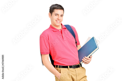 Photo: Smiling student holding books and leaning against wall Smiling student holding books and leaning against wall