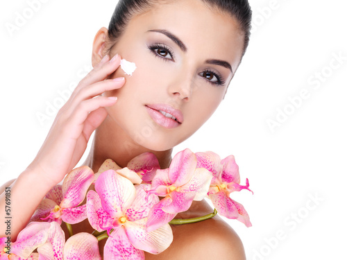 Photo: woman applying cosmetic cream on face with pink flowers on body woman applying cosmetic cream on face with pink flowers on body