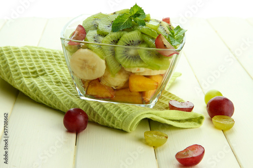 Photo: Tasty fruit salad in glass bowl, on white wooden table Tasty fruit salad in glass bowl, on white wooden table