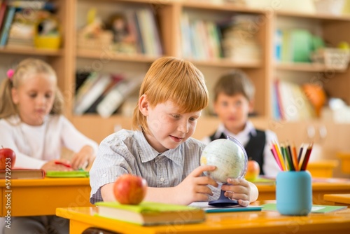 Photo: Little redhead schoolboy behind school desk during lesson Little redhead schoolboy behind school desk during lesson