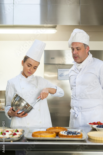 Photo: Frowning chef whisking while being watched by head chef Frowning chef whisking while being watched by head chef