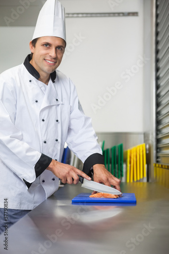 Photo: Smiling chef cutting raw salmon with knife on blue cutting board Smiling chef cutting raw salmon with knife on blue cutting board