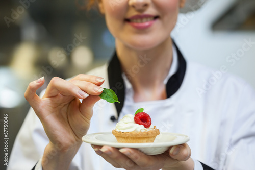Photo: Happy head chef putting mint leaf on little cake on plate Happy head chef putting mint leaf on little cake on plate