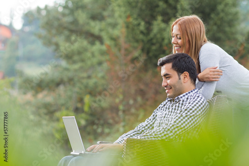 Photo: Couple or friends using laptop, outdoor - outside Couple or friends using laptop, outdoor - outside