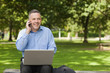 Photo : Happy professor talking on phone while sitting on bench using laptop on campus Happy professor talking on phone while sitting on bench using laptop on campus