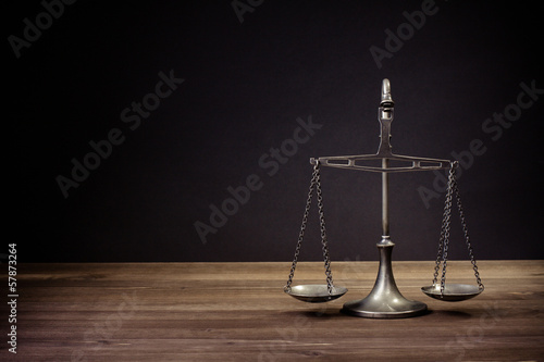 Photo: Law scales on table in front black background. Symbol of justice Law scales on table in front black background. Symbol of justice