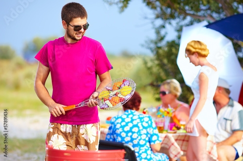 Photo: happy man prepares food on the grill, family picnic happy man prepares food on the grill, family picnic