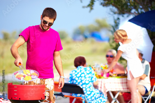 Photo: happy man cooks vegetables on the grill, family picnic happy man cooks vegetables on the grill, family picnic