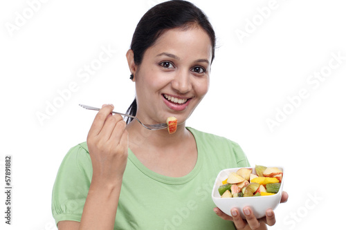 Photo: Young Indian woman eating fruit salad against white Young Indian woman eating fruit salad against white