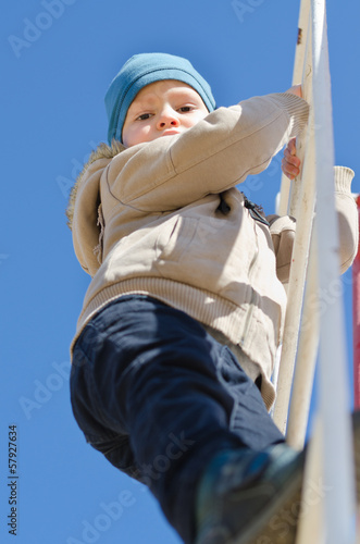 Photo: Cute active child climbing up a ladder in the park Cute active child climbing up a ladder in the park