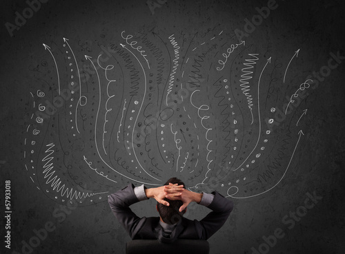 Photo: Businessman thinking with sketched arrows in front of a chalkboa Businessman thinking with sketched arrows in front of a chalkboa