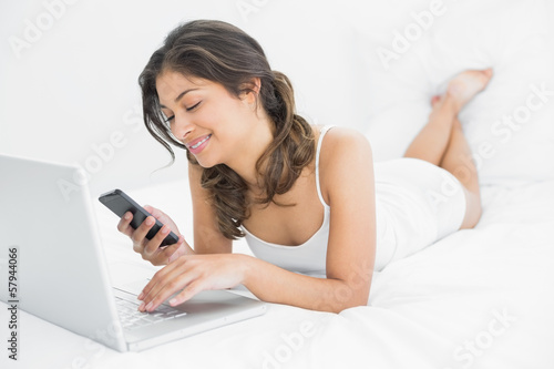 Photo: Casual woman using laptop while text messaging in bed Casual woman using laptop while text messaging in bed