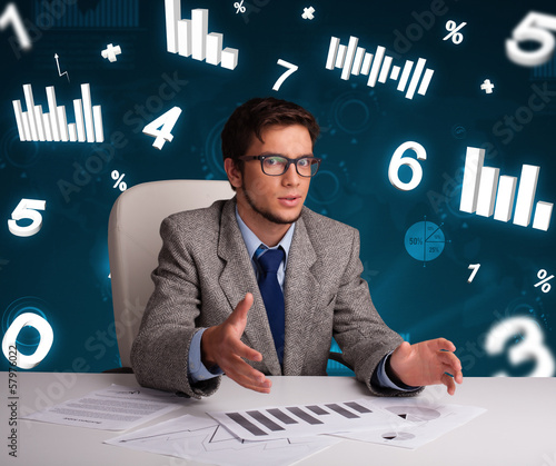 Photo: Businessman sitting at desk with diagrams and statistics Businessman sitting at desk with diagrams and statistics