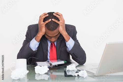 Photo: Frustrated Afro businessman with head in hands at desk Frustrated Afro businessman with head in hands at desk