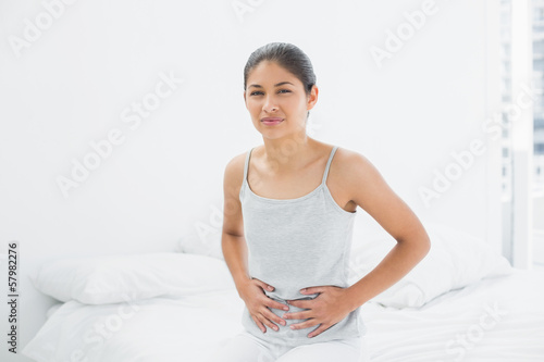 Photo: Casual woman with stomach pain sitting in bed Casual woman with stomach pain sitting in bed