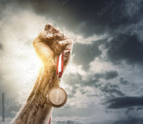 Photo: Success, male hand holding gold medal against the dramatic sky Success, male hand holding gold medal against the dramatic sky