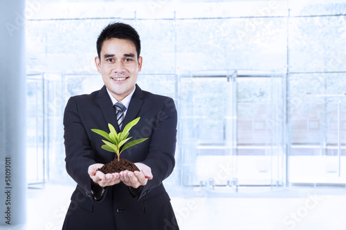Photo: Smiling businessman holding a plant Smiling businessman holding a plant