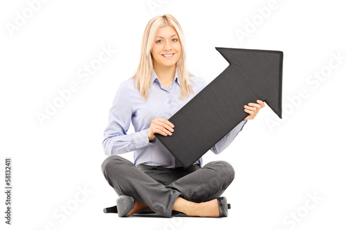 Photo: Young blond woman seated on a floor holding a big black arrow Young blond woman seated on a floor holding a big black arrow