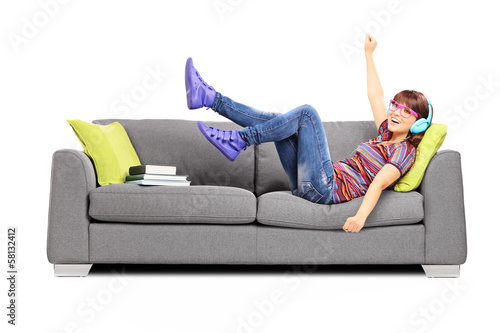 Photo: Young excited female listening music seated on a sofa Young excited female listening music seated on a sofa