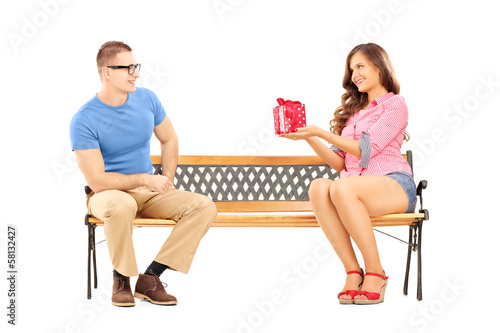 Photo: Young female giving a gift box to her boyfriend, on a bench Young female giving a gift box to her boyfriend, on a bench