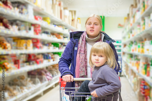 Photo: Mother with daughter in shopping cart select products on shelves Mother with daughter in shopping cart select products on shelves