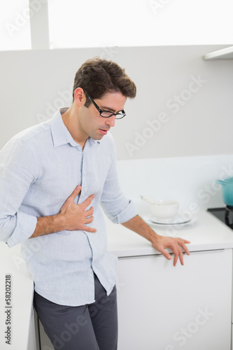 Photo: Casual man with stomach pain standing in the kitchen Casual man with stomach pain standing in the kitchen