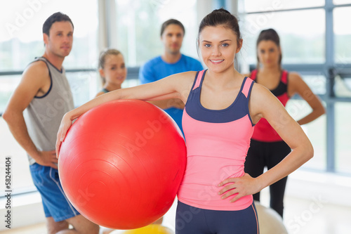 Photo: Instructor holding exercise ball with fitness class in backgroun Instructor holding exercise ball with fitness class in backgroun