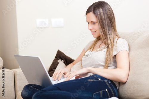 Photo: Smiling woman sitting with laptop on sofa in lounge Smiling woman sitting with laptop on sofa in lounge