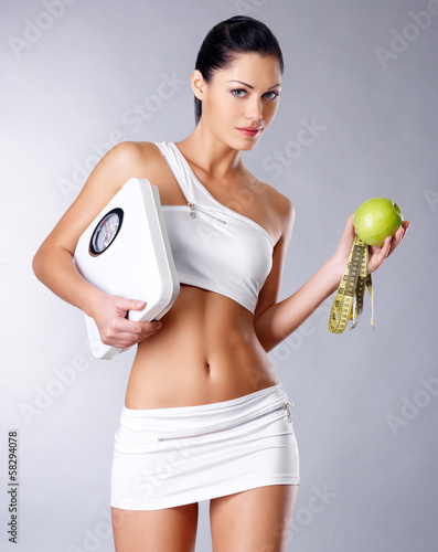 Photo: Healthy woman stands with the scales and green apple. Healthy woman stands with the scales and green apple.