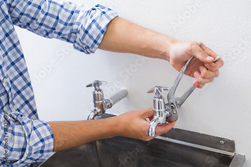 Photo: Plumber hand's fixing water tap with pliers Plumber hand's fixing water tap with pliers