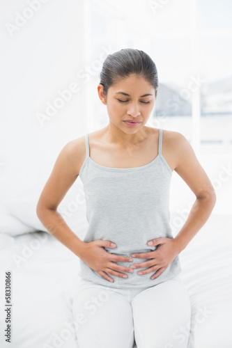 Photo: Casual woman with stomach pain sitting in bed Casual woman with stomach pain sitting in bed