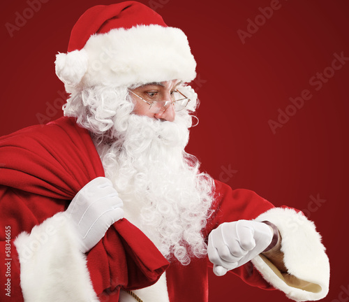 Photo: Santa Claus with a bag of presents and looking at his watch Santa Claus with a bag of presents and looking at his watch