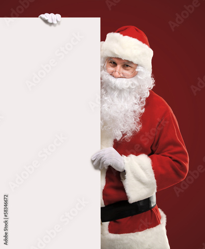 Photo: Santa Claus looking out from behind the blank sign isolated Santa Claus looking out from behind the blank sign isolated