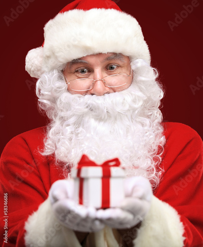 Photo: Santa Claus giving xmas present and looking at camera Santa Claus giving xmas present and looking at camera