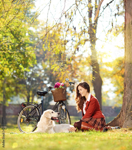 Photo: Pretty female sitting down with her dog in a park Pretty female sitting down with her dog in a park