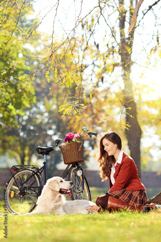 Photo: Pretty female sitting down with her dog in a park Pretty female sitting down with her dog in a park