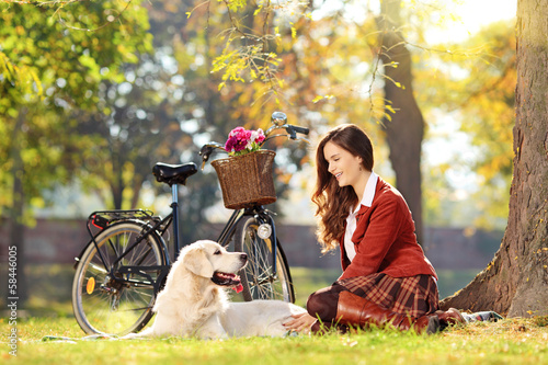 Photo: Beautiful female sitting down on a grass with her dog in a park Beautiful female sitting down on a grass with her dog in a park