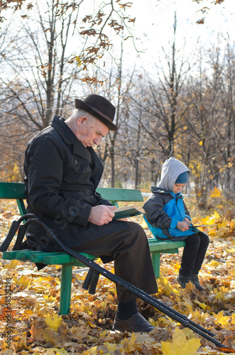 Photo: Retired man reading in the park with his grandson Retired man reading in the park with his grandson