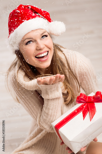 Photo: Happy woman with gift box in Santa hat looking at snowflakes Happy woman with gift box in Santa hat looking at snowflakes