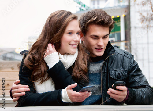 Photo: Young couple being outside on the phone and text messaging Young couple being outside on the phone and text messaging