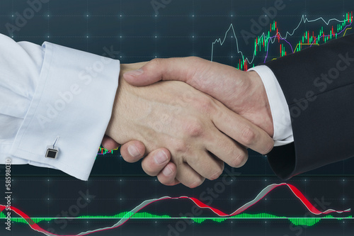 Photo: Handshake over stock market graph. Handshake over stock market graph.