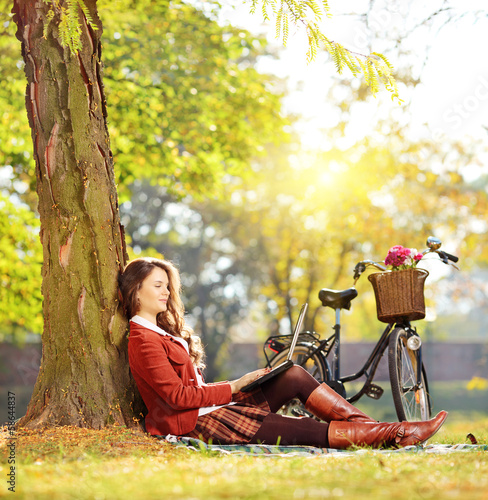 Photo: Young female working on a laptop seated on a grass in a park Young female working on a laptop seated on a grass in a park