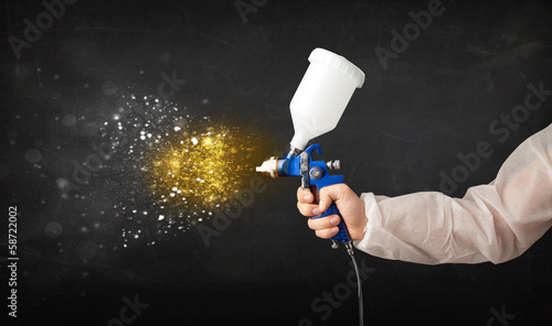 Photo: Worker with airbrush painting with glowing golden paint Worker with airbrush painting with glowing golden paint