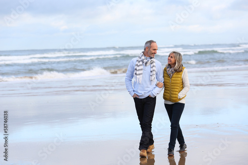 Photo: Senior couple walking on the beach in winter time Senior couple walking on the beach in winter time