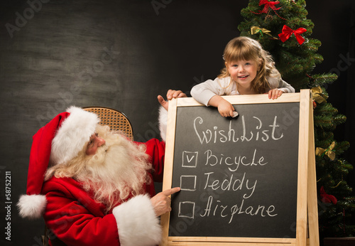 Photo: Santa Claus with child sitting near chalkboard with wish list an Santa Claus with child sitting near chalkboard with wish list an