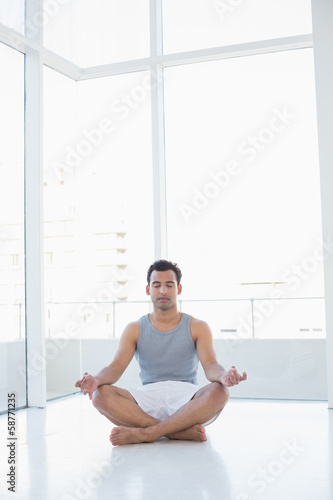 Photo: Full length of a young man sitting in lotus pose Full length of a young man sitting in lotus pose