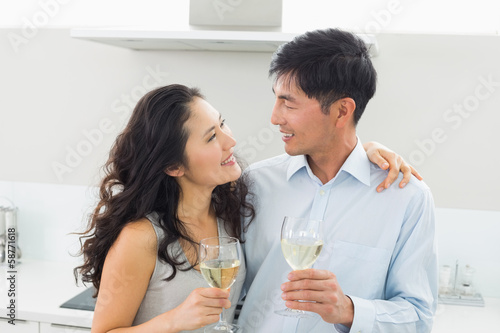 Photo: Loving young couple with wine glasses in kitchen Loving young couple with wine glasses in kitchen