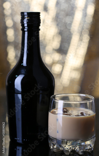 Photo: Baileys liqueur in bottle and glass on golden background Baileys liqueur in bottle and glass on golden background