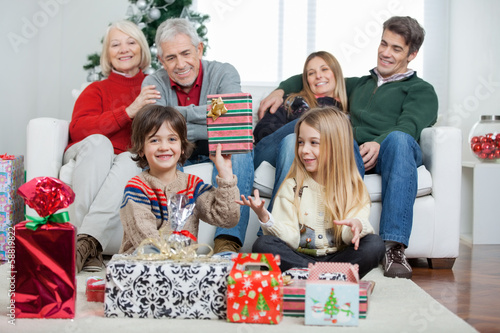 Photo: Boy Holding Christmas Gift With Family In House Boy Holding Christmas Gift With Family In House
