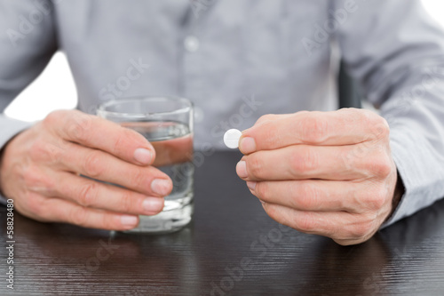 Photo: Mid section of a man holding glass of water and pill Mid section of a man holding glass of water and pill